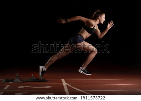 Woman Sprinter in Action Bursting From Blocks During Race, black background Royalty-Free Stock Photo #1811573722