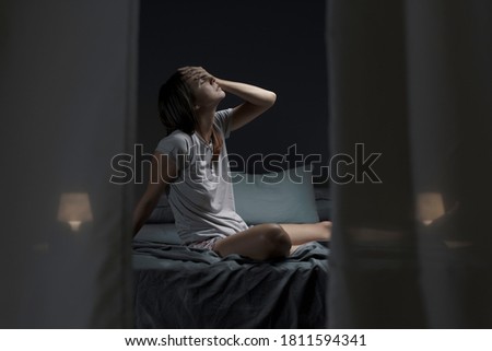 Tired woman sitting in bed at night with open window, she is suffering from the heat and she is unable to sleep Royalty-Free Stock Photo #1811594341