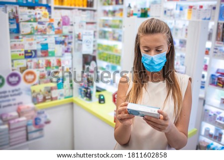 Charming young woman shopping at pharmacy. Attractive female customer shopping for medical goods at local pharmacy. Purchase, retail concept. Shelves of medicine are in the background. 
