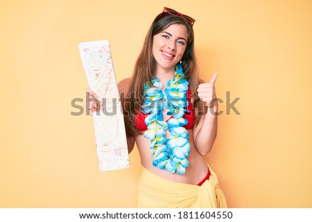 Beautiful young caucasian woman wearing bikini and holding city map smiling happy and positive, thumb up doing excellent and approval sign 