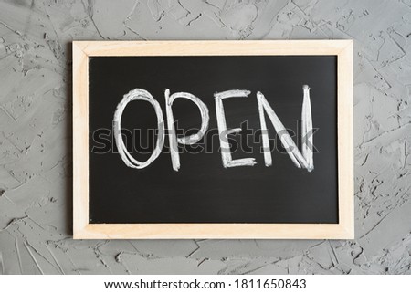 Word "Open" written on a blackboard, concrete wall as background. Open sign for cafes, bars, small shops and stores