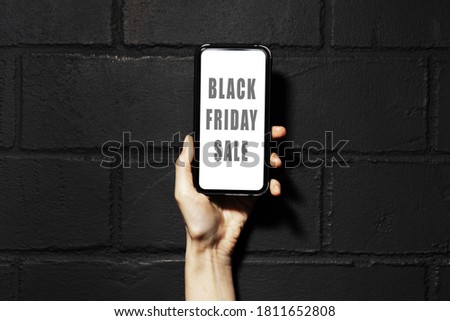 Black friday sale text on screen of smartphone in female hand. Background of black brick wall.