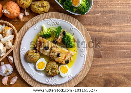 Cod loin baked in olive oil, with potatoes, broccoli, boiled egg and black olives. Typical dish of Portugal. Top view. Space for text.