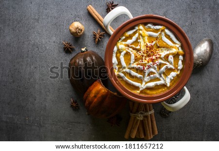 Spicy squash soup in ceramic pot. Halloween dinner top view photo. Dark grey background with copy space. 
