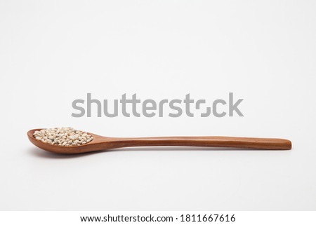 Wooden spoon with unhulled barley on white
