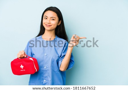 Young chinese nurse woman isolated on a blue background touching back of head, thinking and making a choice.