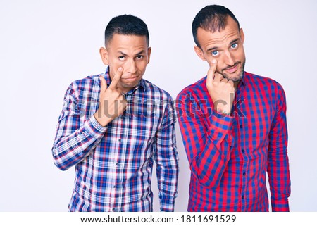 Young gay couple of two men wearing casual clothes pointing to the eye watching you gesture, suspicious expression 