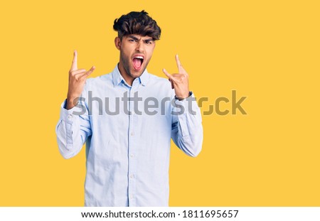 Young hispanic man wearing casual shirt shouting with crazy expression doing rock symbol with hands up. music star. heavy concept. 