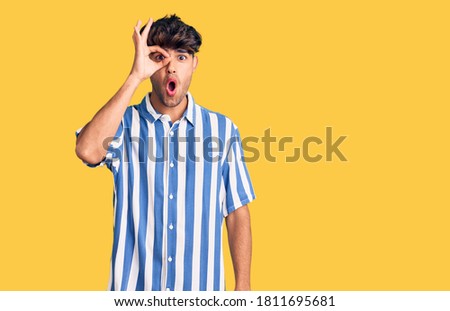 Young hispanic man wearing casual clothes doing ok gesture shocked with surprised face, eye looking through fingers. unbelieving expression. 