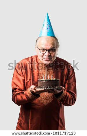 Indian old man celebrating own birthday by blowing candles on cake while wearing ethnic wear