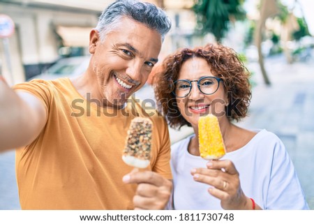 Middle age couple eating ice cream and making selfie by the camera at street of city.