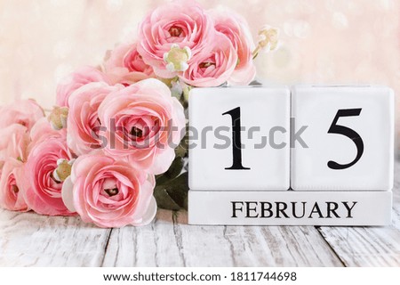 White wood calendar blocks with the date February 15th for International Childhood Cancer Awareness Day and pink ranunculus. Selective focus with blurred background.