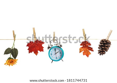 Set your clocks back with this clock, flower, autumn leaves and and pine cone hanging by clothes pins to a clothes line over a white background. Daylight saving time concept. Clipping path included.
