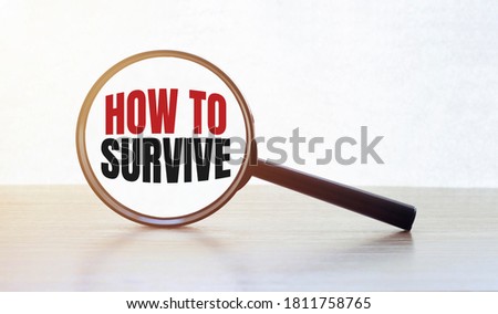 Magnifying glass with text HOW TO SURVIVE on wooden table.
