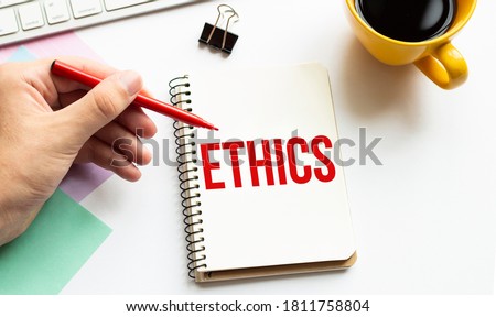 Hand with red pen. Cofee cup. Stick. Keyboard and white background. ETHICS sign in the notepad