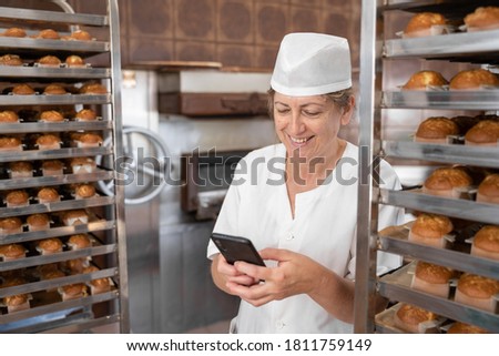 Baker woman smiling and texting with her phone surrounded by cupcakes
