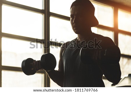 Silhouette picture of a man performing exercises with dumbbells in the gym. Strength training
