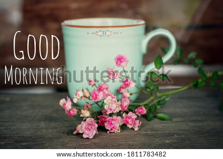 Morning greeting text message with a cup of morning coffee or tea and little pink roses flower on the table. Good Morning.