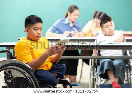 asian disabled children(lost legs) using tablet and sitting on a wheelchair in classroom Royalty-Free Stock Photo #1811792959