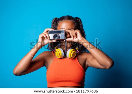 Young beautiful black woman taking pictures with retro vintage photo camera on blue background - Diverse female isolated studio shot holding camera - photography, technology, memories concept