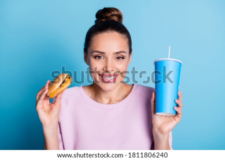 Photo of positive cheerful girl hold hamburger cold takeaway soda glass wear violet jumper isolated over blue color background