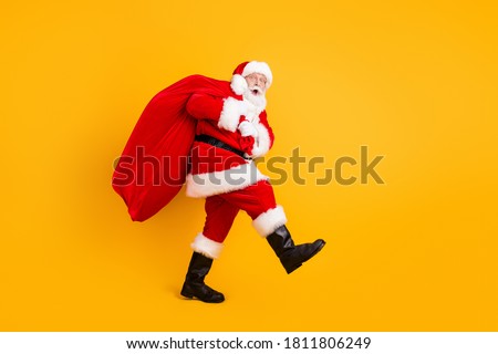 Full length body size profile side view of his he nice funny cheery amazed white-haired Santa carrying big large sack custom tradition isolated bright vivid shine vibrant yellow color background