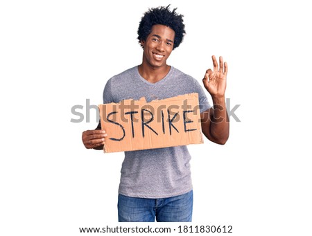 Handsome african american man with afro hair holding strike banner cardboard doing ok sign with fingers, smiling friendly gesturing excellent symbol 