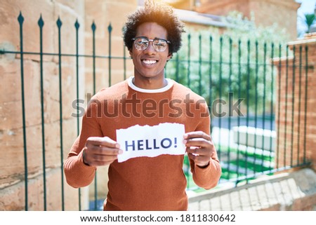 Young handsome african american man smiling happy. Standing with smile on face holding hello message paper at town street.