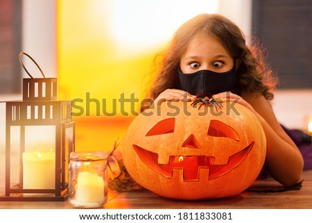 A funny girl looks with surprise at a spider on an orange pumpkin