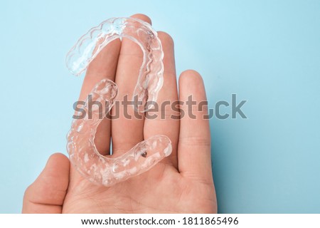 Close up mans hand holding invisible aligners for whitening and straightening of teeth on the blue background. Orthodontic therapy after brackets. Teeth healthcare Royalty-Free Stock Photo #1811865496