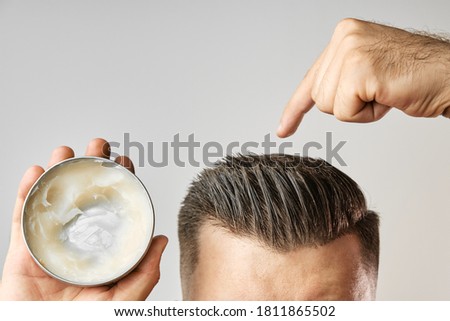 Man applying a clay, pomade, wax, gel or mousse from round metal box for styling his hair after barbershop hair cut. Advertising concept of mans products. Treatment and care against lost of hair Royalty-Free Stock Photo #1811865502