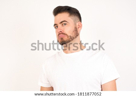 Beautiful man with snobbish expression curving lips and raising eyebrows, looking with doubtful and skeptical expression, suspect and doubt. Standing indoors over white background. Royalty-Free Stock Photo #1811877052
