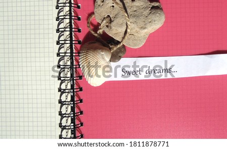 Notebook with white and red pages, stone and shell. On a white strip of paper it says Sweet Dreams.