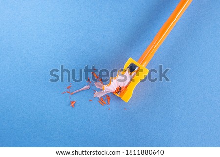 Orange wooden pencil with shavings in a stationery sharpener on a blue background. Creative concept of drawing, creativity, learning. Minimalism, copy space.