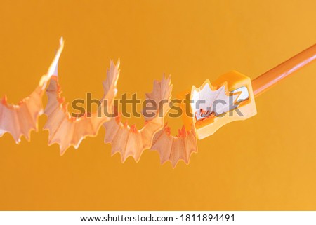 Orange wooden pencil with shavings in a stationery sharpener on an orange background. Monochrome image. Creative concept of drawing, creativity, learning. Minimalism, copy space.