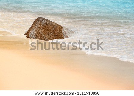 Solid rock in the waves on golden beach, gentle waves floating around, shallow depth of field
