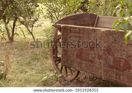 Old styled ancient wooden cart with retro colored woolen dingy carpet stands in the garden between green trees