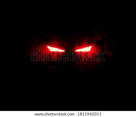 Ominous luminous eyes staring out of the darkness illuminate with rays of red light swirling white smoke Royalty-Free Stock Photo #1811942011