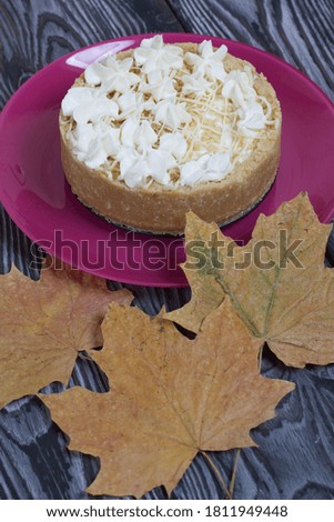 Cheesecake with white chocolate. Nearby are dried maple leaves. On pine planks painted black and white.