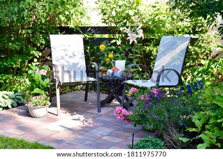 Outdoor summer brick patio with comfortable seating and table for relaxing with a book in the afternoon and al fresco dining in the evening Royalty-Free Stock Photo #1811975770