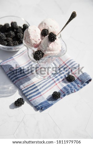 A bowl of ice cream and blackberries sits on a blue checkered napkin. Close up.Vertical orientation.