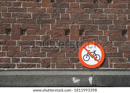 Bicycle parking prohibited, a red, round, metal sign leaned on a brick wall in the old city of Rotterdam, Netherlands, Europe.          