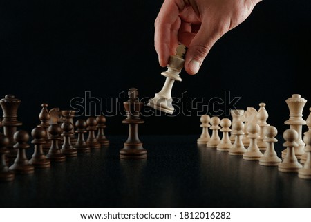hand holding chess piece king on black background with other chess figures
