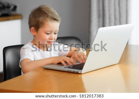 A young boy using a laptop computer sitting on top of a tableundefined at home
