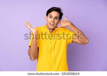 Man over isolated purple background making phone gesture and doubting