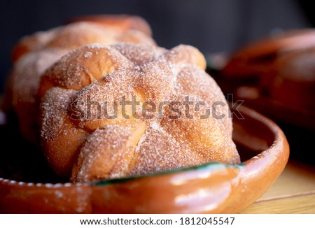 Exquisite traditional pan de muerto or bread of dead decorated with sugar above on a traditional clay plate on a table black background and mexican style. Royalty-Free Stock Photo #1812045547