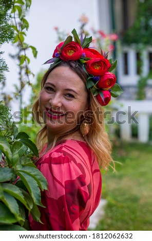Beautiful attractive creative cheerful woman wearing pink dress and headband of rose flowers is posing and dancing outdoors at the villa house in the green beautiful garden.