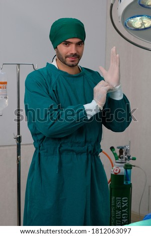 A team surgeons prepare themself for performing an operation, handsome young doctor wearing head protecting cloth uniform in a modern operating room.