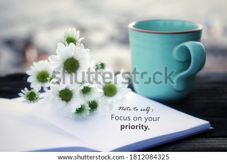 Note to self. Focus on your priority. Self motivation concept on flat lay vintage background with white daisy flowers and blue cup of morning coffee or tea on the table.