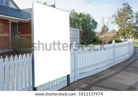 Blank white mockup template of a real estate advertisement billboard/sign/board at front of a property/residential house with white wood picket fence in an Australian suburb. 